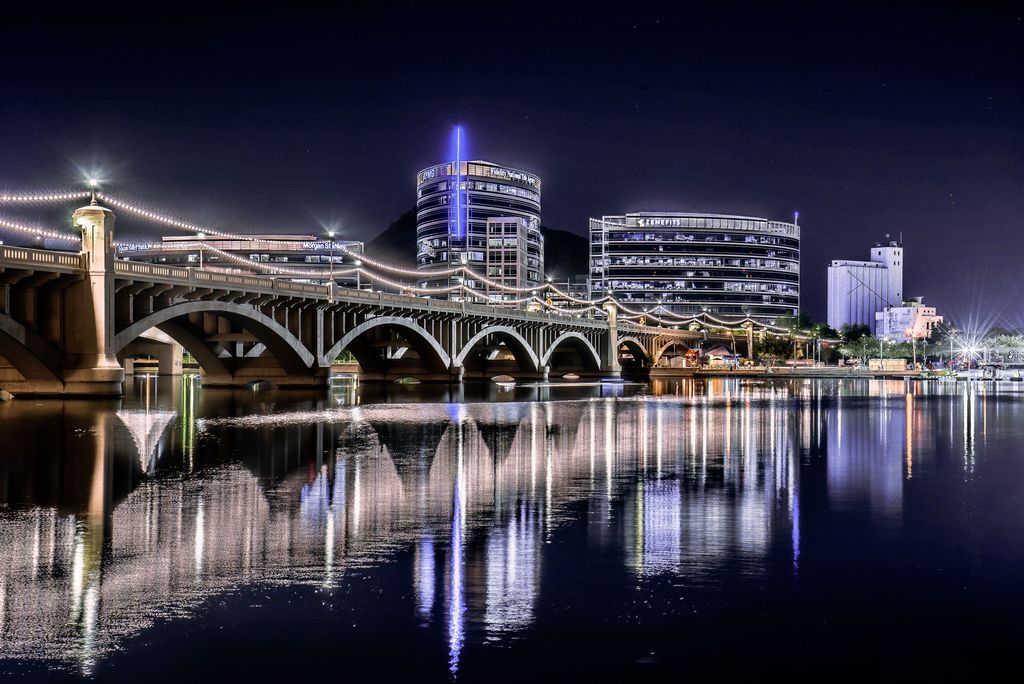Tempe Town Lake bridge and downtown Tempe buildings lit up at night, reflected in the water
