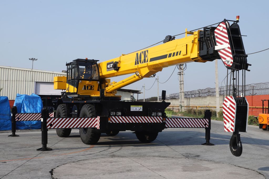 Yellow rough-terrain crane set up on extended outriggers in an industrial yard