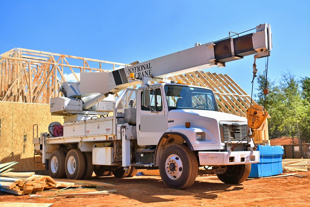 White boom truck parked beside timber roof trusses on a construction site