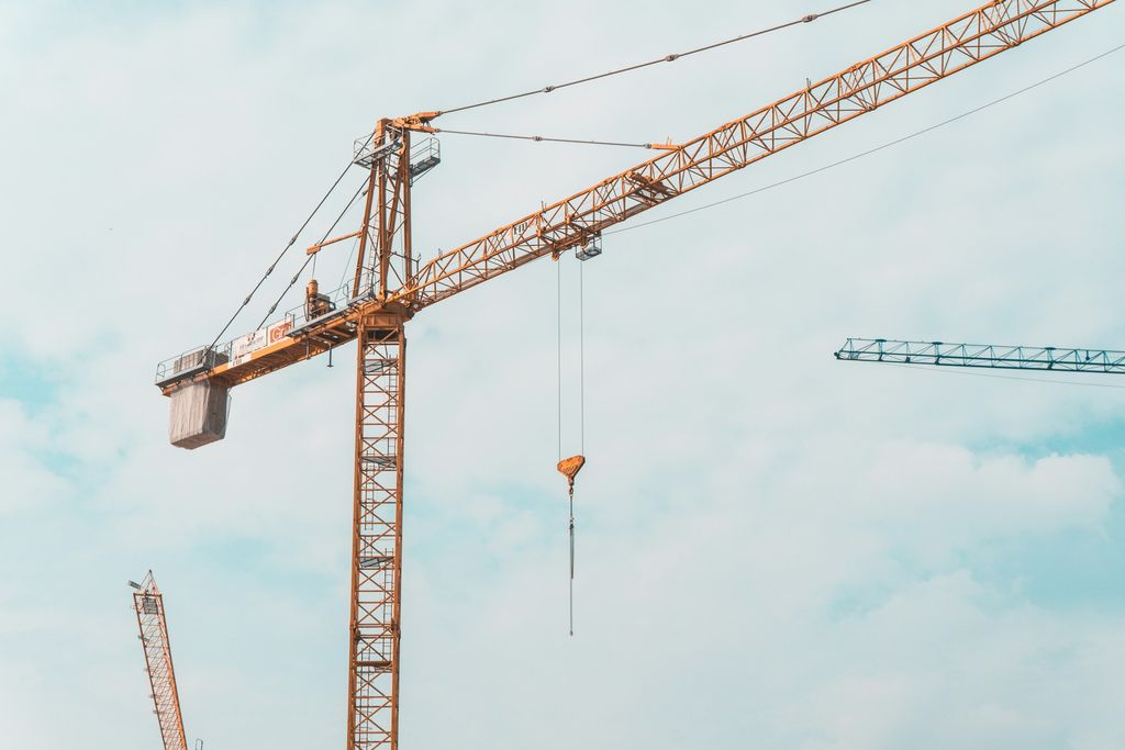 Tower crane jib and hook against a pale sky above a construction site